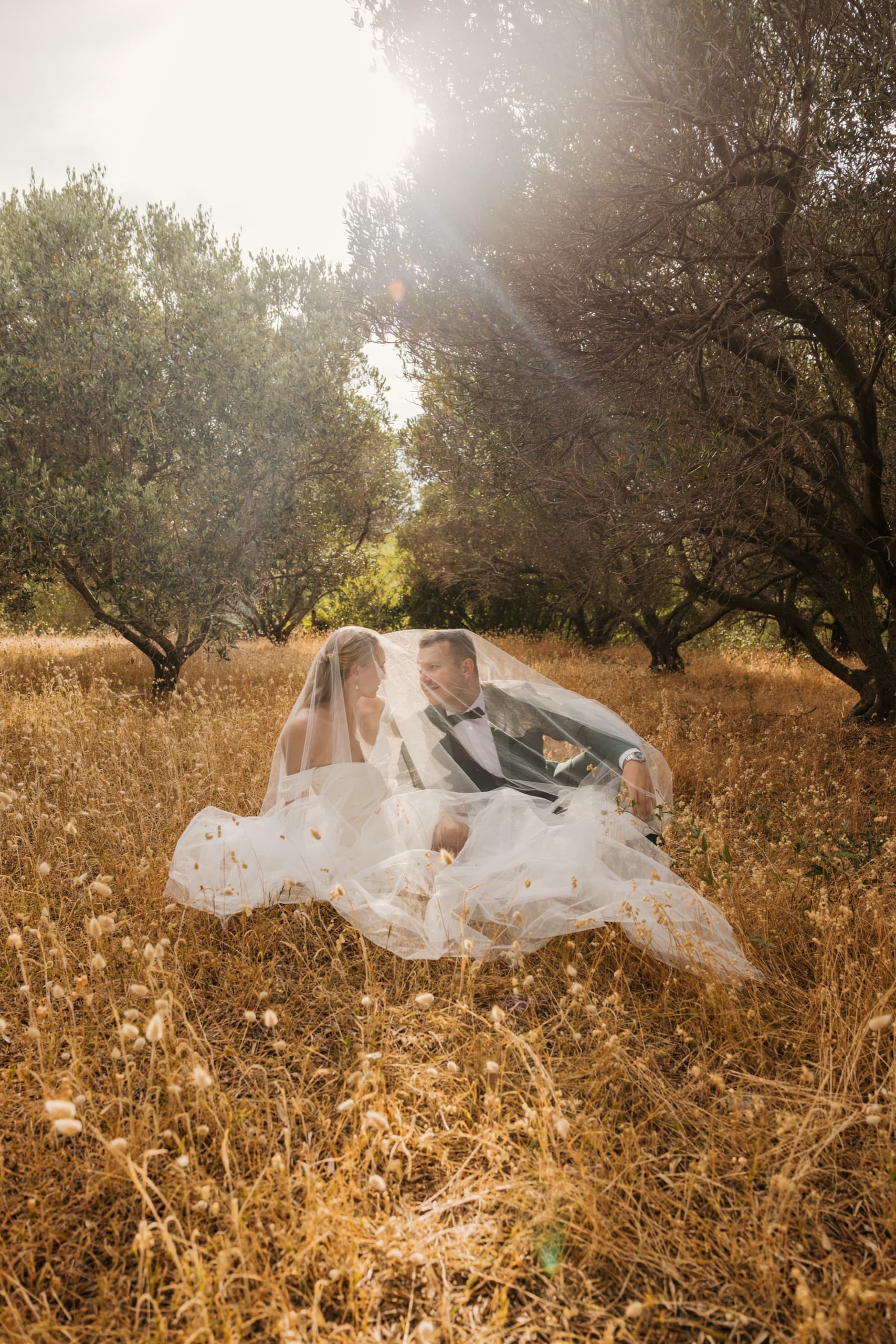 Bride lying in a sunlit golden field, her veil spread around her
