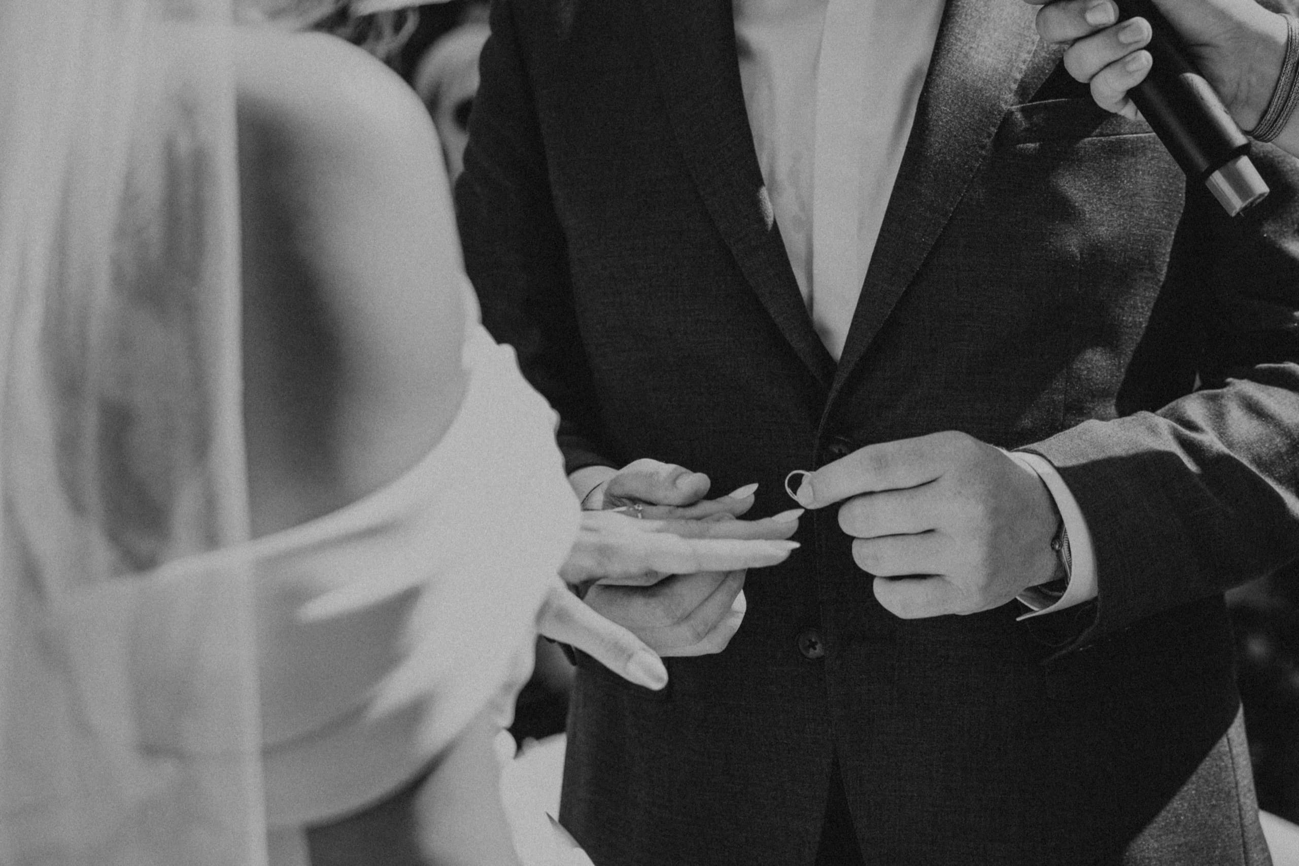 Groom fastening his jacket beside the bride’s veil, black and white