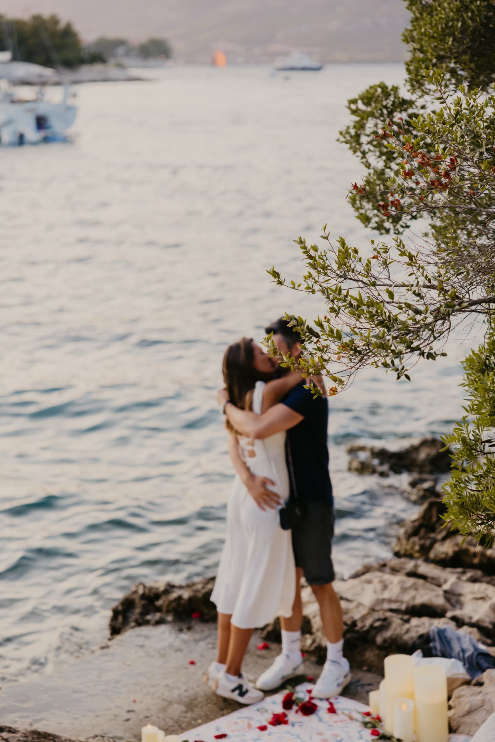 A couple embracing at the water’s edge as boats drift past