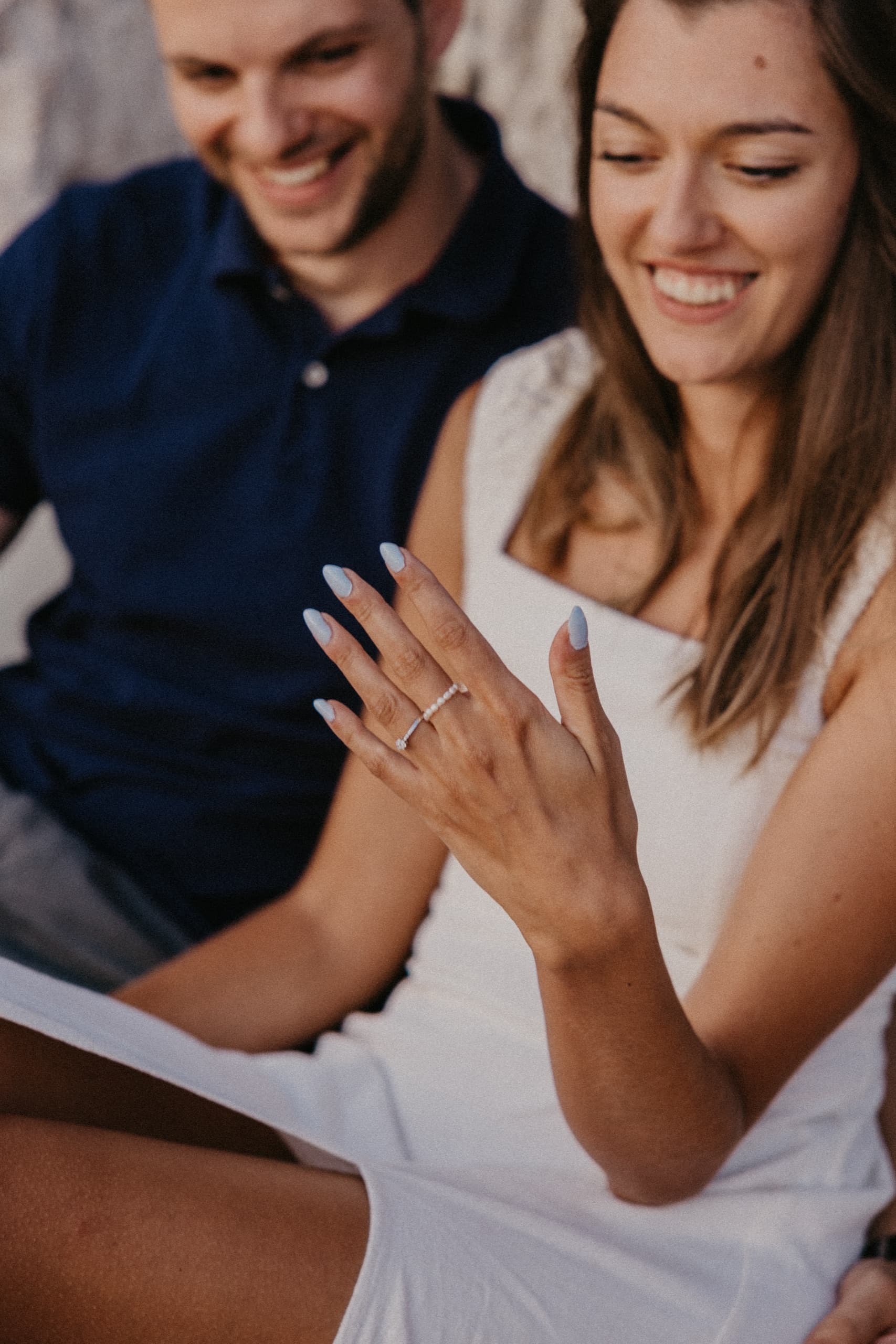 A newly engaged couple laughing as she shows her ring